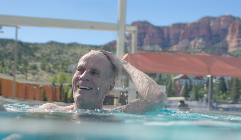 A senior man swims in the goldstream pool with redrock landscaping in the background.