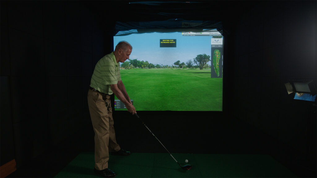 A senior man plays golf in a virtual simulator.
